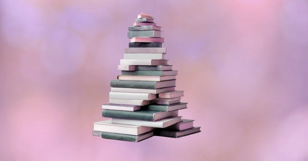 A tall, pyramid-shaped stack of notebooks in muted shades of pink, green, and white against a soft, blurred pink background